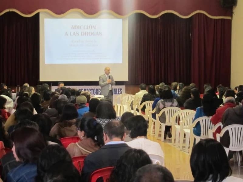 Auditorio lleno de padres de familia frente a la proyección titulada «Adicción a las drogas»