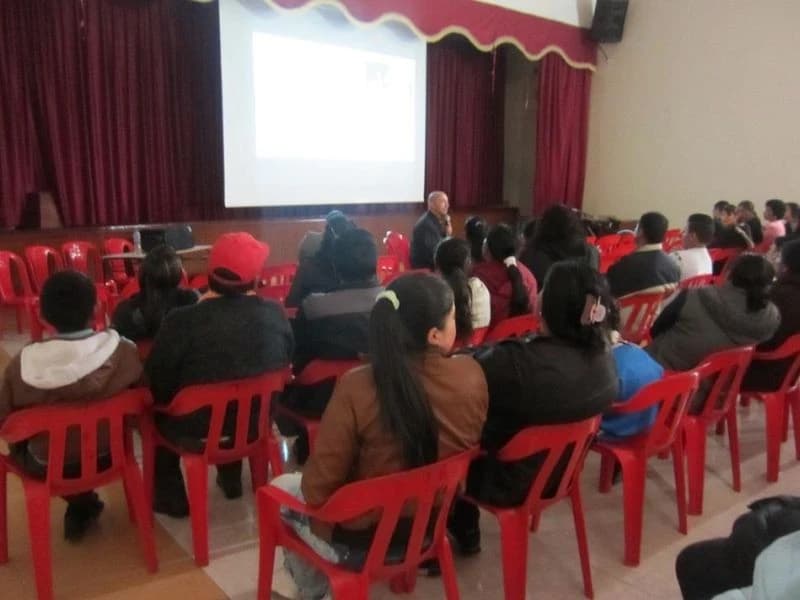 Salón con sillas rojas ocupadas y la presentación proyectada al fondo