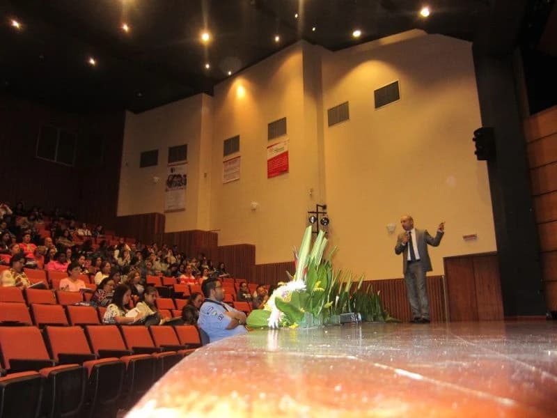 Conferencista en la tarima de un teatro con la platea ocupada