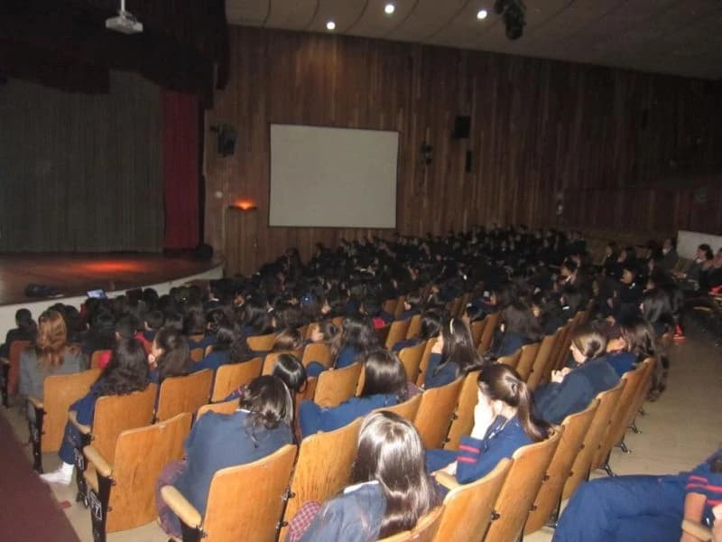 Auditorio de sillas naranjas lleno de estudiantes y padres de familia
