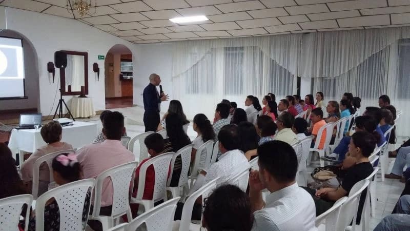 Público numeroso frente al conferencista en un salón amplio con cortinas